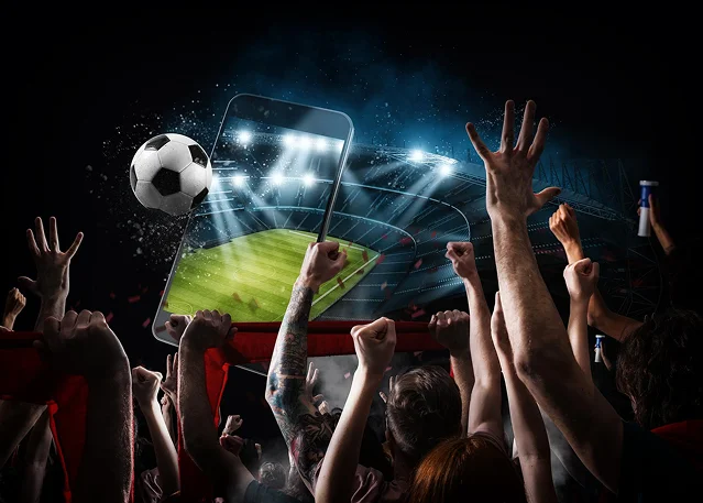 Fãs de futebol entusiasmados a celebrar num estádio enquanto assistem a um jogo ao vivo no ecrã de um dispositivo móvel
